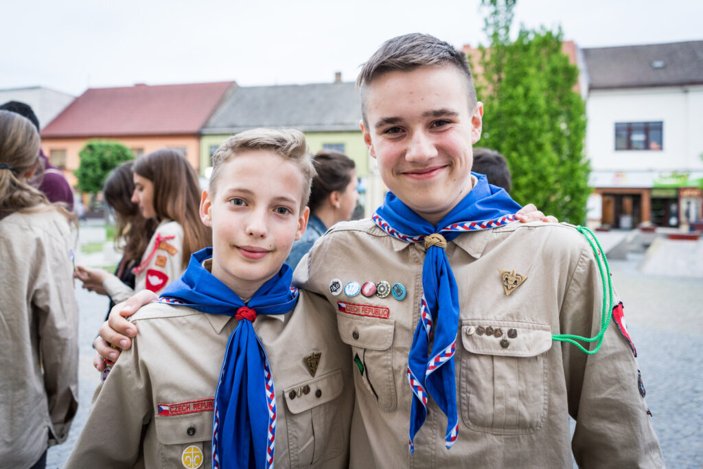 Dvaja usmievajúci sa skauti v rovnošatách s modrými šatkami, jeden má ruku na pleci druhého.